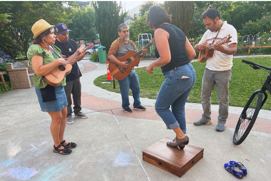 caption: Iris Viveros Avendaño doing zapateado, percussive dancing, on the tarima while other Seattle Fandango Project members play Son Jarocho music.