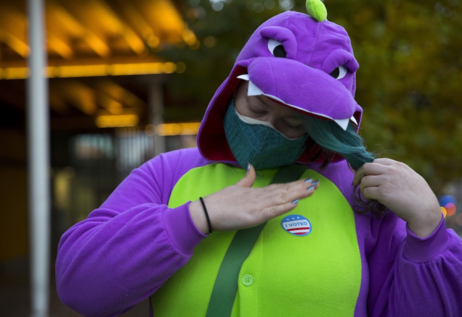caption: King County voter Petri Muhlhauser puts an 'I Voted' sticker on her dinosaur costume after voting outside of the Seattle Public Library Ballard Branch on Tuesday, November 3, 2020, in Seattle.