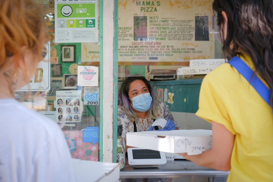 caption: Veronica Delgado, masked, hands pizza to customers through the order window at Hot Mama's Pizza, August 2, 2021. Staff at Hot Mama's discussed no longer wearing masks when the mandate was lifted but ultimately decided to keep wearing them due to continued and uncertainty and safety concerns.