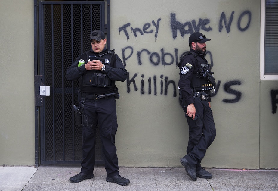 caption: Security guards stand in front of graffiti that reads 'they have no problem killing us,' as the Capitol Hill Organized Protest zone, CHOP, is cleared on Wednesday, July 1, 2020, in Seattle. 