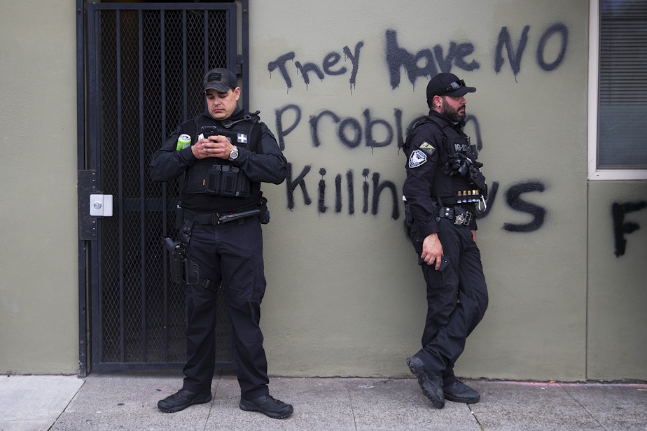 caption: Security guards stand in front of graffiti that reads 'they have no problem killing us,' as the Capitol Hill Organized Protest zone, CHOP, is cleared on Wednesday, July 1, 2020, in Seattle. 