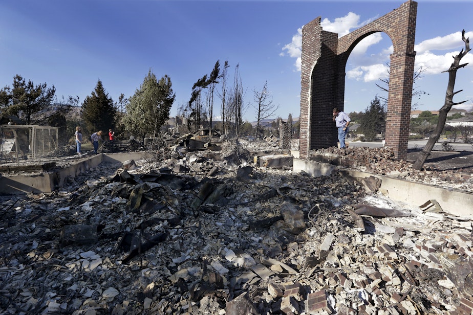 caption: Vern Smith, right, looks across at the rubble of his home, destroyed in a wildfire the night before, Monday, June 29, 2015, in Wenatchee, Wash. The wildfire fueled by high temperatures and strong winds roared into town Sunday afternoon. The blaze ignited in brush just outside Wenatchee, quickly burning out of control. 