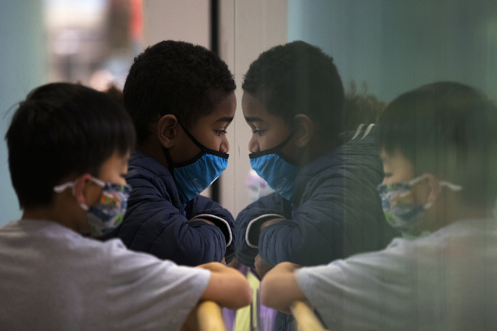 caption: Lucas Tham, 7, left, and Kiran Dick, 7, look through a pane of glass to another floor of Seattle Children's Hospital while waiting to receive Covid-19 vaccines on Tuesday, November 9, 2021, in Seattle.