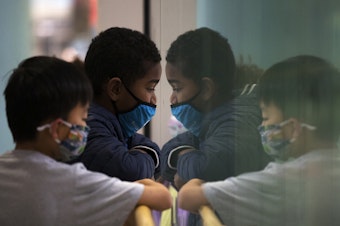 caption: Lucas Tham, 7, left, and Kiran Dick, 7, look through a pane of glass to another floor of Seattle Children's Hospital while waiting to receive Covid-19 vaccines on Tuesday, November 9, 2021, in Seattle.