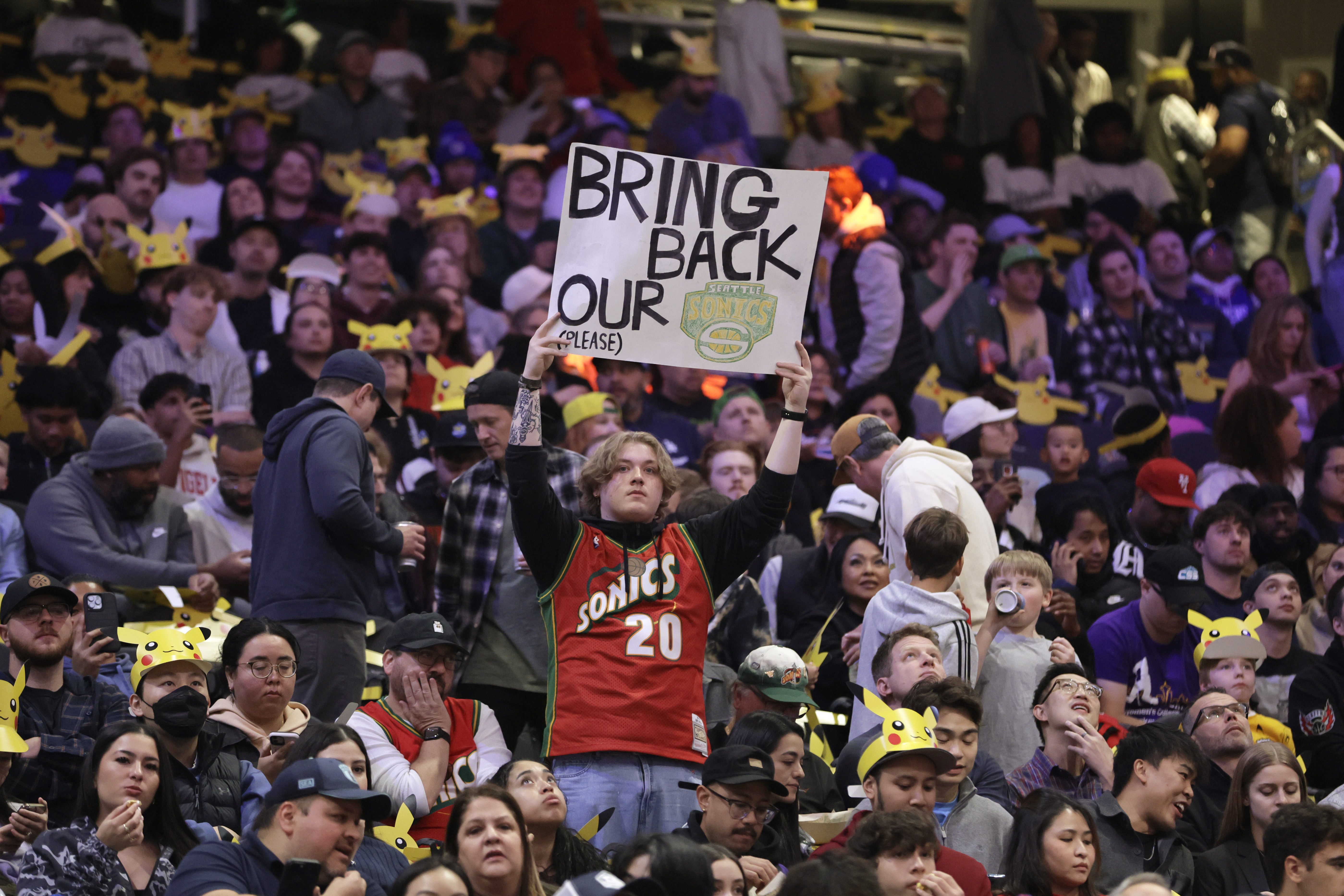 caption: A fan hold up a sign in the stands urging the former Seattle Sonics basketball team to return to Seattle before a preseason NBA basketball game between the Los Angeles Clippers and the Portland Trail Blazers, Friday, Oct. 11, 2024, in Seattle. 
