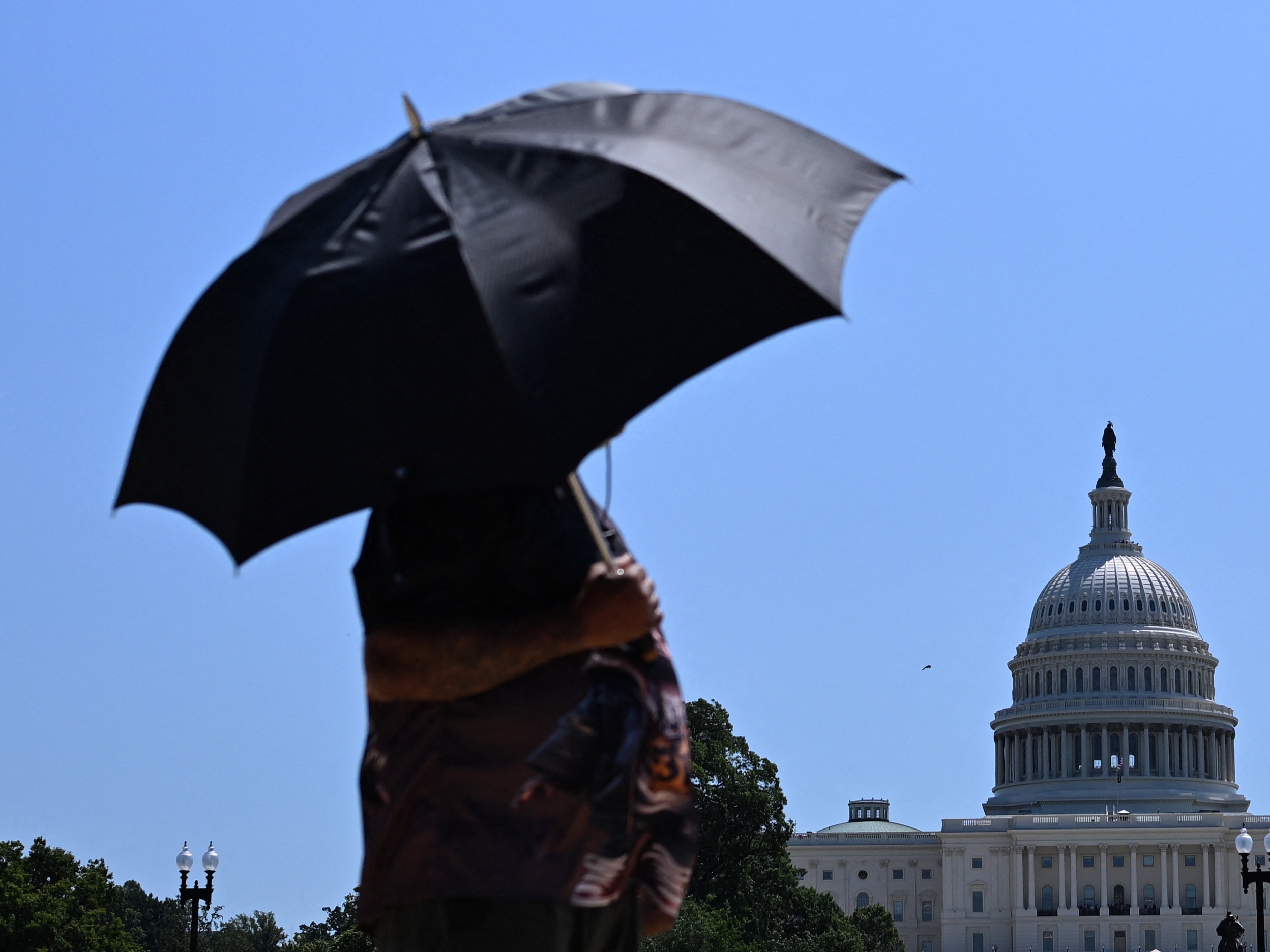 caption: A person uses an umbrella as they walk near Capitol Hill in Washington, D.C., on Friday. The United States is experiencing its first significant heat wave of the year, across the Great Plains and expanding into parts of the Midwest and Great Lakes over the weekend, according to the National Weather Service.