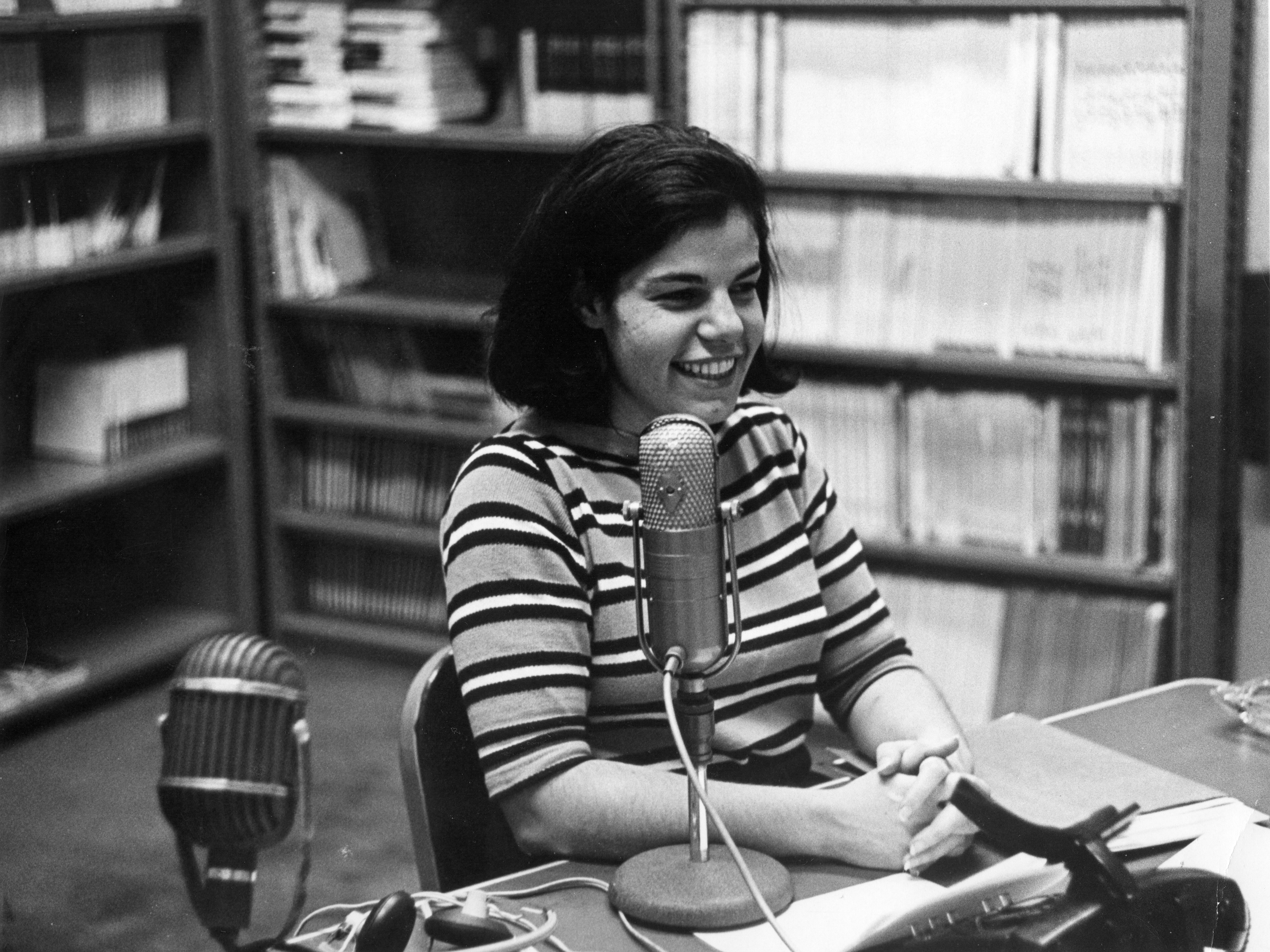 caption: Susan Stamberg at a microphone, age 25. Later, as the host of <em>All Things Considered,</em> she was the first woman to be a full-time anchor of a U.S. national nightly news broadcast.