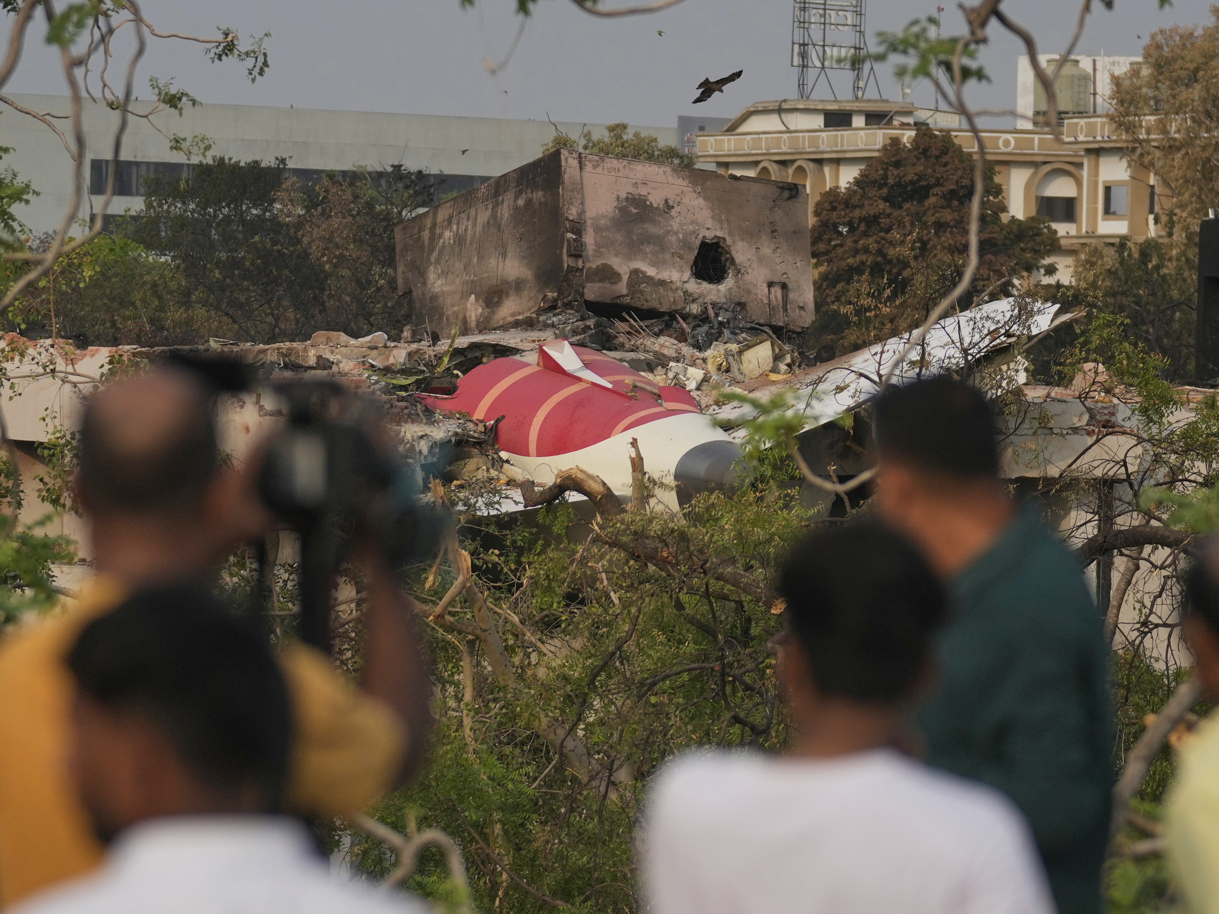 caption: Onlookers watch wreckage from Thursday's Air India plane crash lying atop a building in Ahmedabad, India, on Saturday.