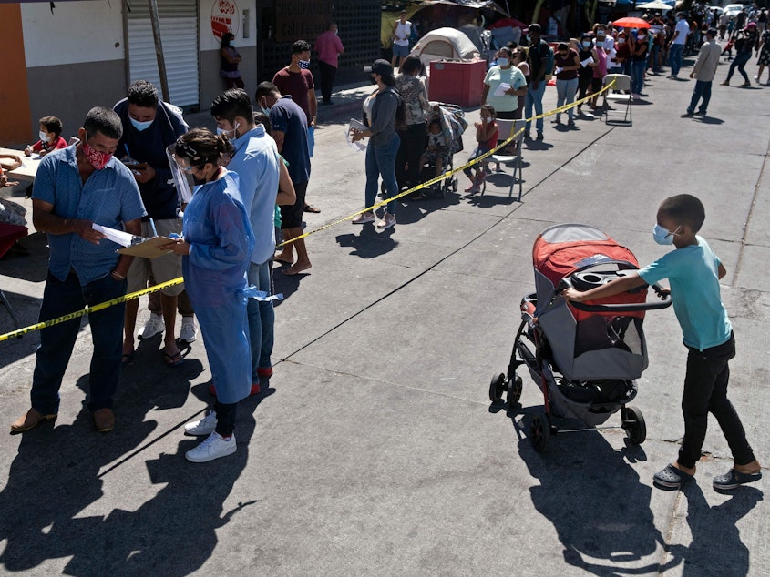caption: Asylum seekers camping at El Chaparral crossing port queue to be vaccinated against COVID-19 last month in Tijuana, Mexico, on the border with the U.S.