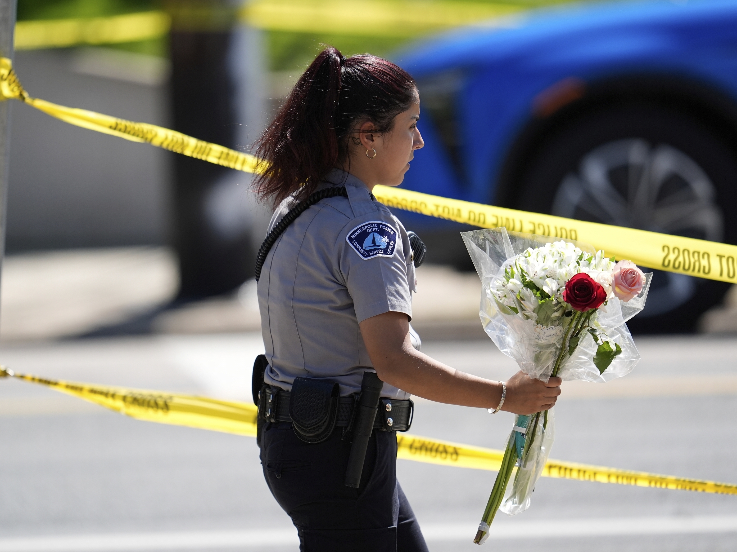 caption: A police officer carries flowers outside the Annunciation Church's school after the shooting on Wednesday in Minneapolis.