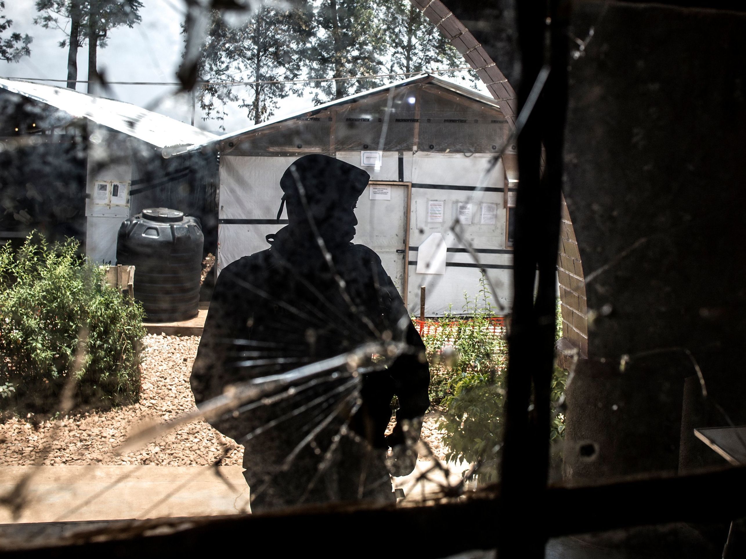 caption: A police officer stands guard by a window riddled with bullet holes in an Ebola treatment center in Butembo, a city in Democratic Republic of the Congo. The center has been attacked twice in the last month.
