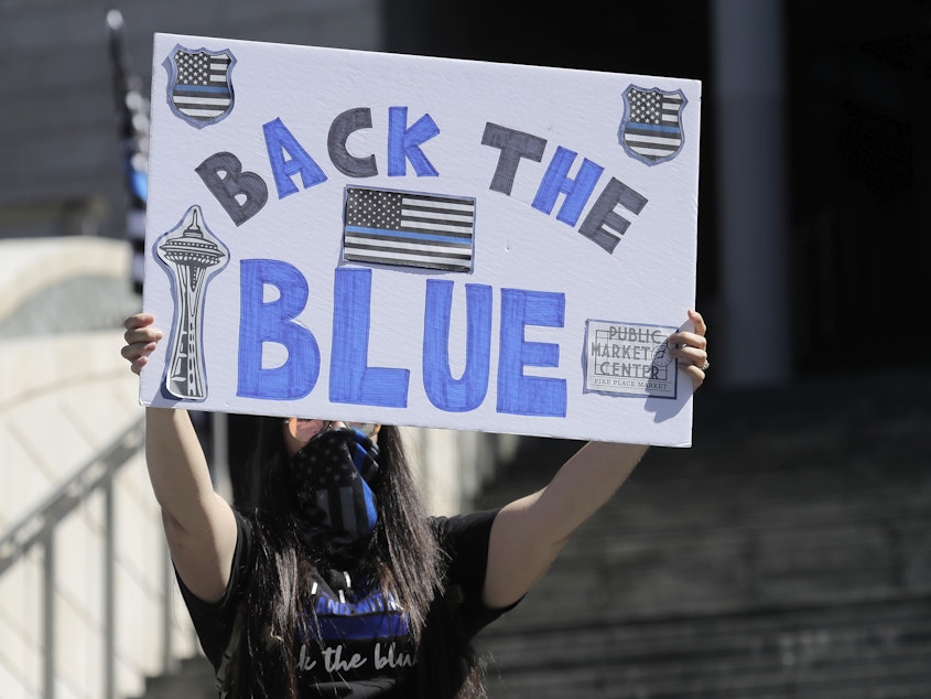 caption: A person holds a "Back the Blue" sign in support of police during a 2020 rally in front of Seattle City Hall.