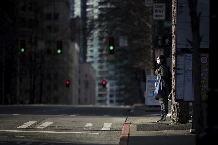 caption: A pedestrian waits to cross Third Avenue on Wednesday, March 25, 2020, in Seattle.