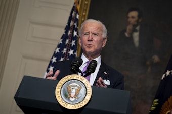 caption: President Biden speaks about the coronavirus pandemic in the State Dining Room of the White House on Tuesday.