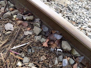 caption: A discarded hypodermic needle next to the train tracks outside the Yankee Diner on Shilshole Avenue in Ballard, Seattle.