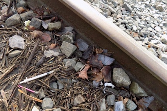 caption: A discarded hypodermic needle next to the train tracks outside the Yankee Diner on Shilshole Avenue in Ballard, Seattle.