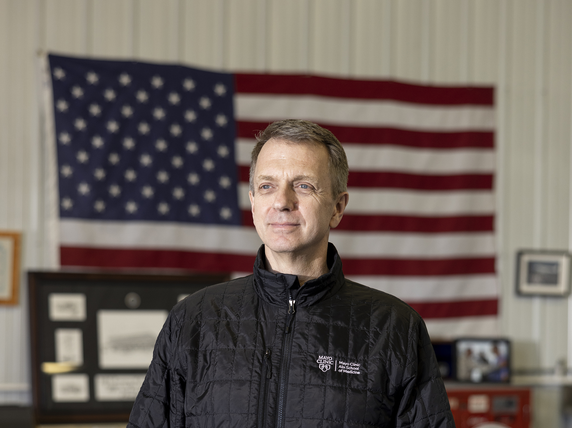 caption: Dr. Todd Rasmussen stands in his home office in Rochester, Minn. He is a former combat surgeon who did six tours in Iraq and Afghanistan.