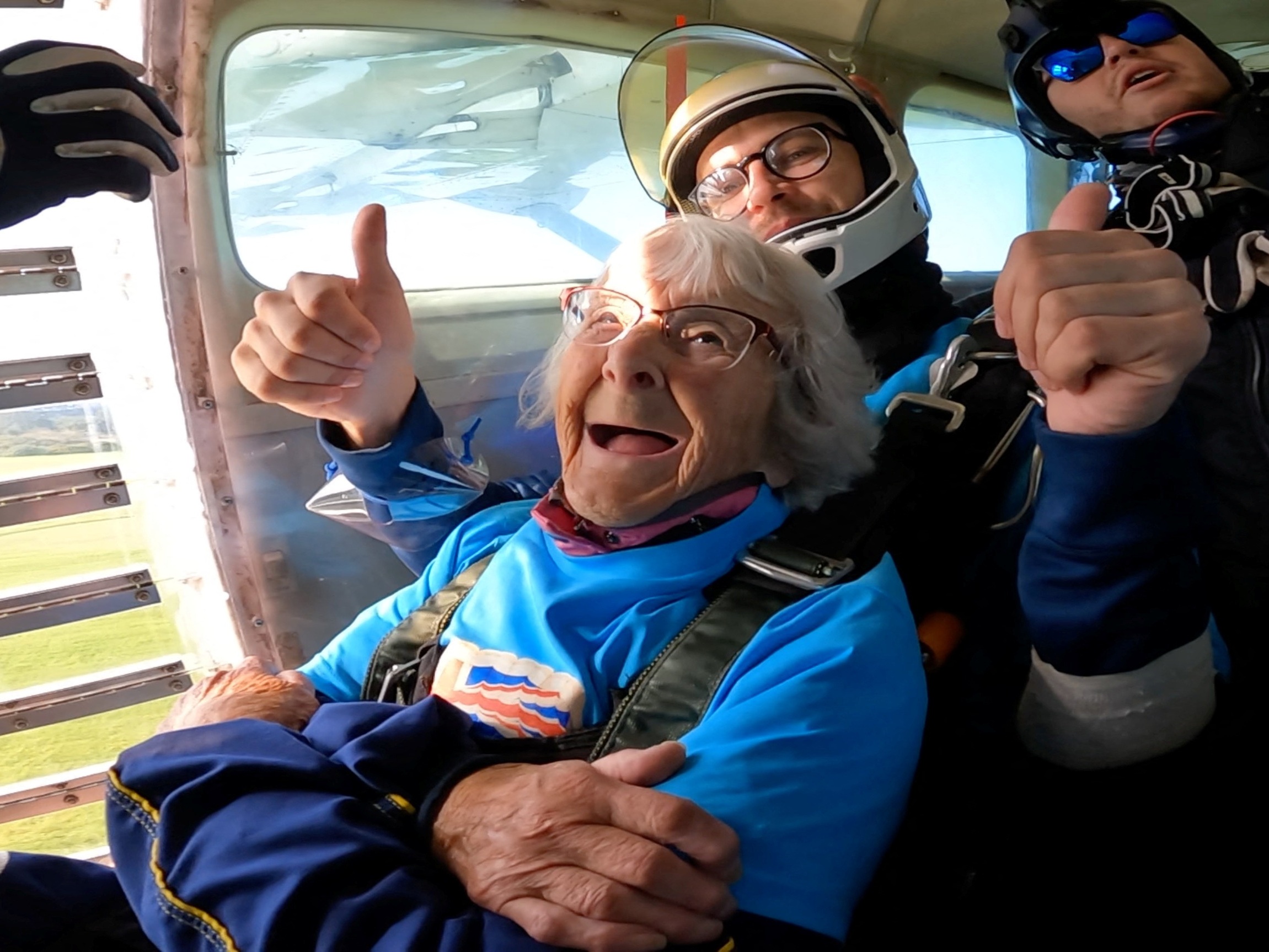 caption: In this screengrab taken from a handout video, Manette Baillie, 102, smiles as she prepares to skydive over England on Sunday.