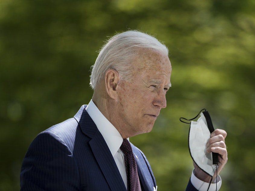 caption: President Biden removes his mask before speaking about the pandemic outside of the White House on Tuesday afternoon.
