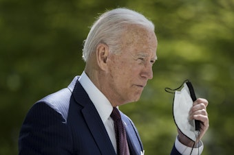 caption: President Biden removes his mask before speaking about the pandemic outside of the White House on Tuesday afternoon.