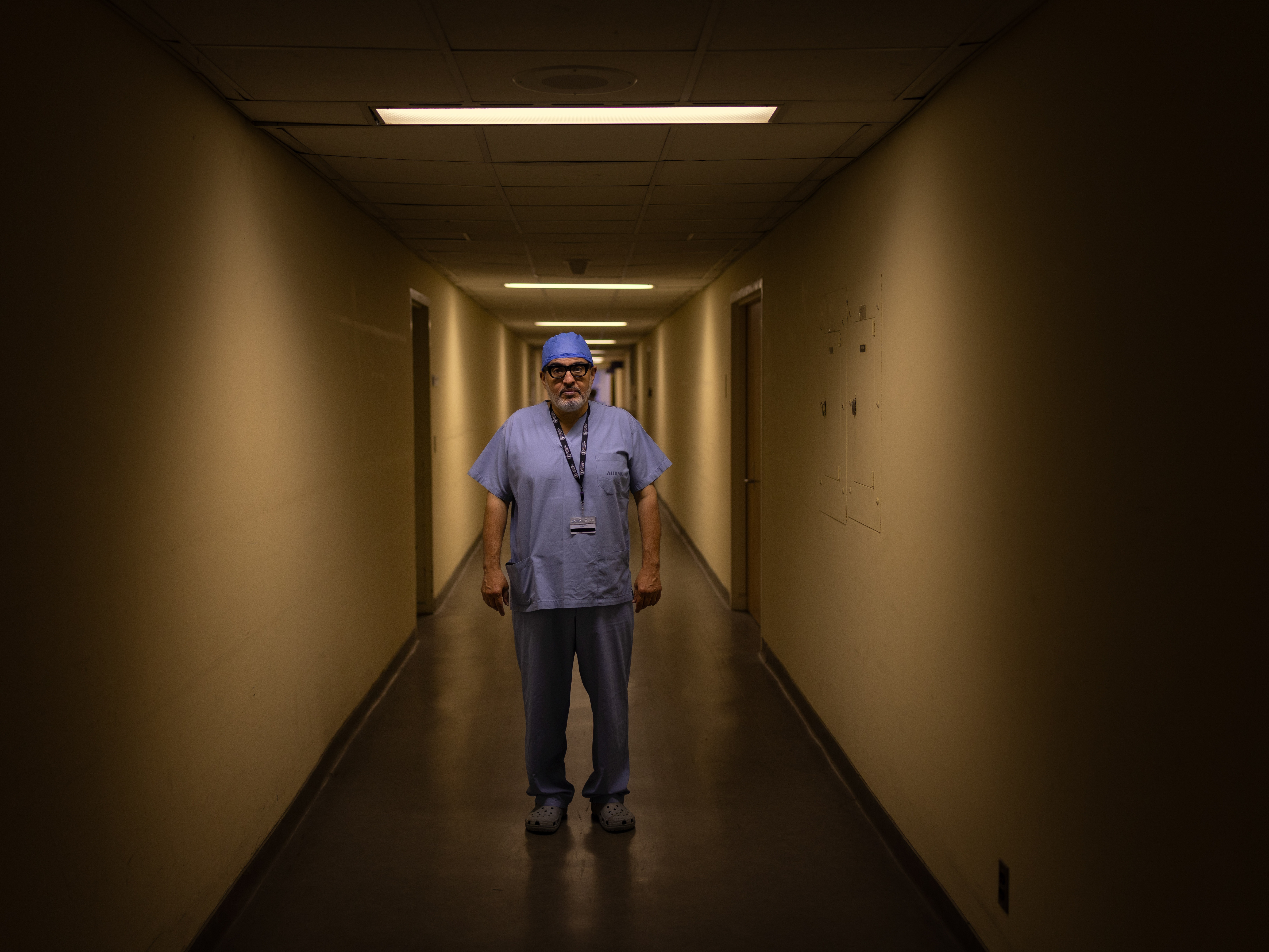 caption: Dr. Ghassan Abu-Sittah stands in a corridor at the American University of Beirut Medical Center. He is a reconstructive and plastic surgeon who treats those wounded in war, including, by his estimate, thousands of children.