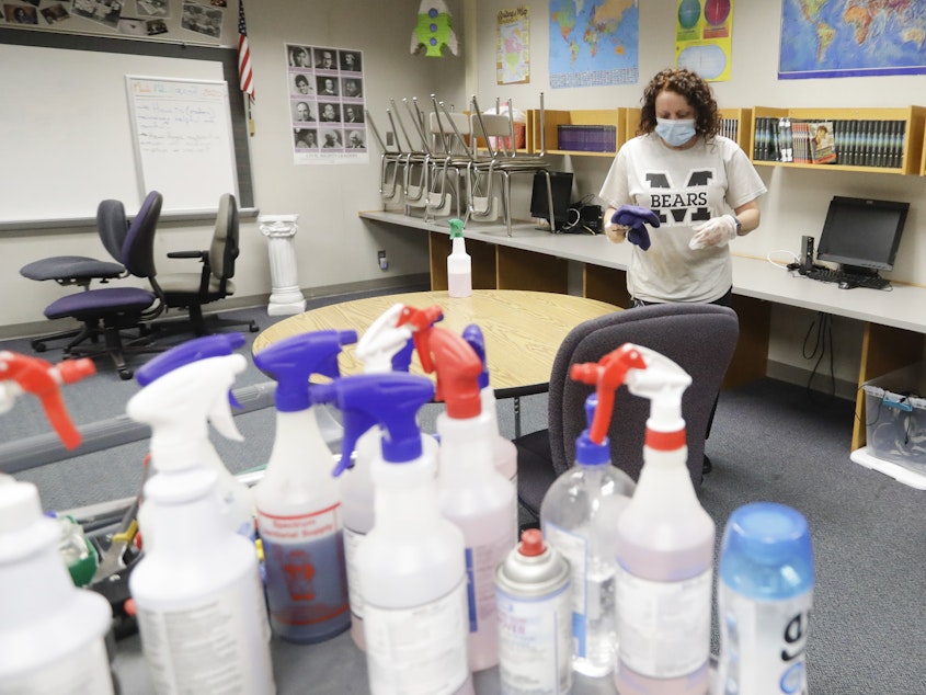 caption: Charo Woodcock cleans a classroom at McClelland Elementary School in June in Indianapolis. Students across Indiana are already back in school in a mix of in-person and online instruction.