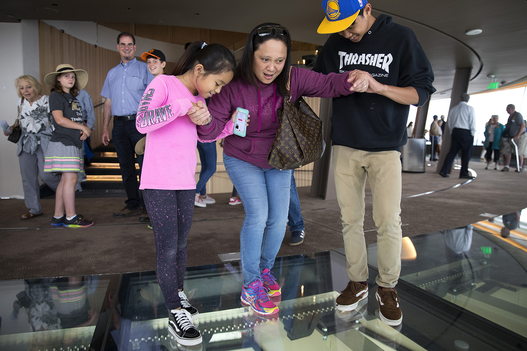caption: Samantha Ramirez, 9, left, and Benjamin Ramirez, 16, right, help their mother, Sheila Ramirez, center, to step onto the rotating glass floor at the Space Needle on Friday, August 3, 2018, in Seattle. 
