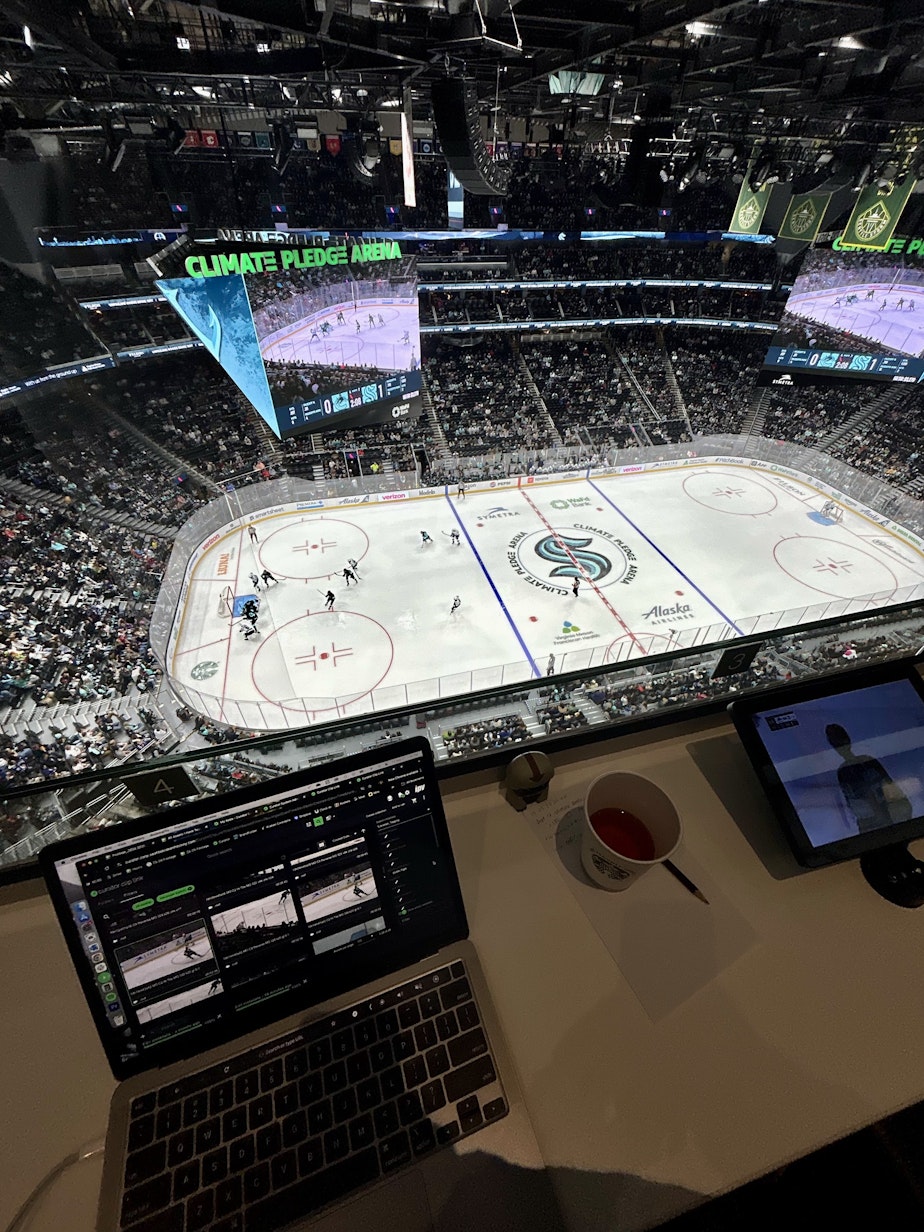 caption: Seattle Kraken digital asset librarian Gina Rome watches a preseason game against the Vancouver Canucks from the press bridge on Sept. 27, 2024. The press bridge provides a great view of the ice, but Rome said people in the bridge aren't supposed to cheer — which is hard for a fan like her.