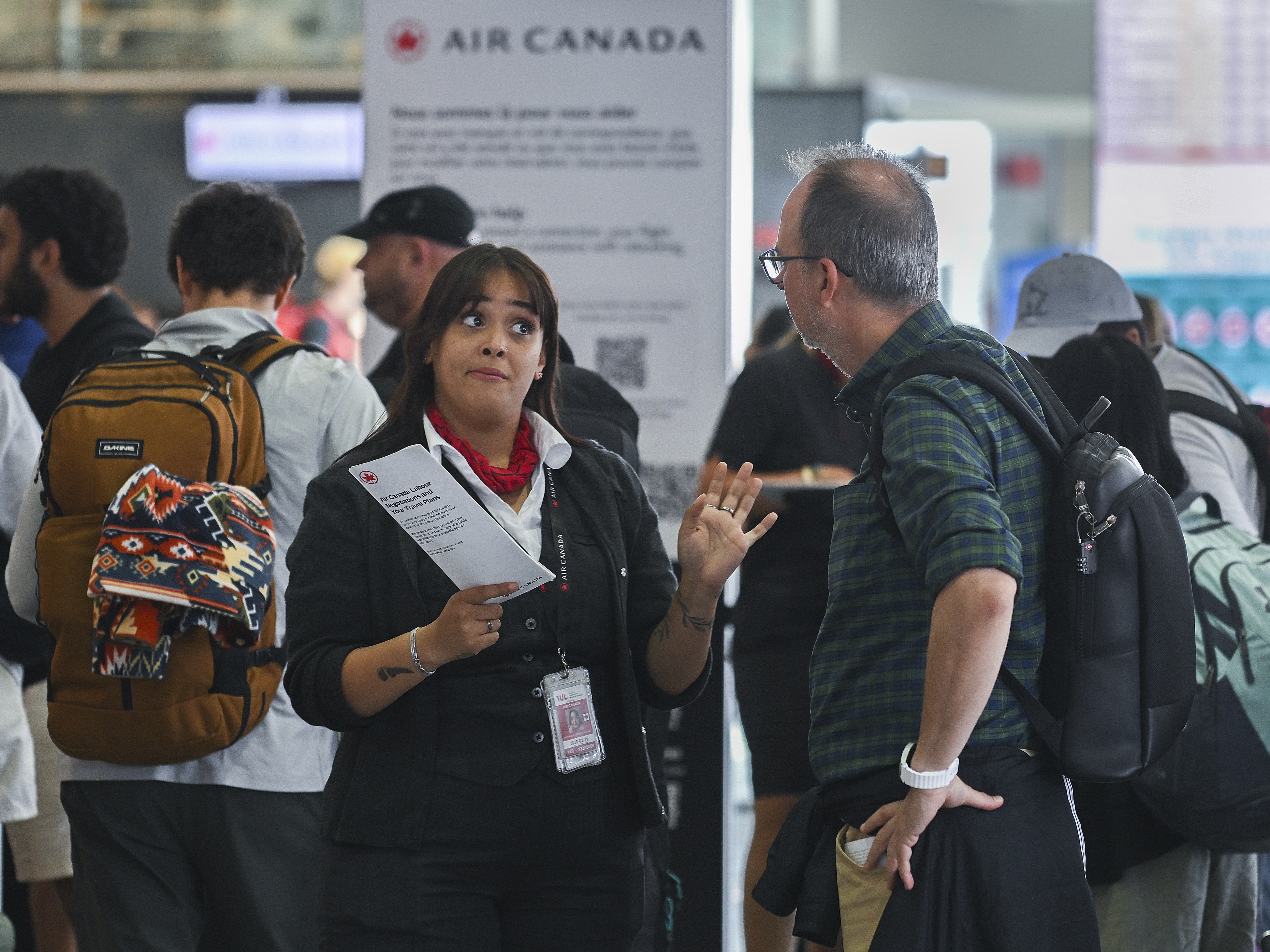 caption: An Air Canada agent, left, talks with a man as Air Canada flight attendants strike at Montreal-Pierre Elliott Trudeau International Airport in Montreal, Saturday, Aug. 16, 2025.