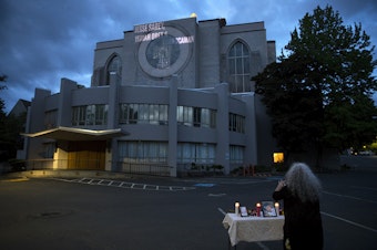 caption: Elaine Simons takes a photograph of a small vigil set up to honor those killed by Auburn police officer Jeffrey Nelson, including her foster son, Jesse Sarey, on Thursday, June 3, 2021, at Saint Mark's Episcopal Cathedral in Seattle. Family members gathered to see their loved ones names projected onto the side of the building as part of the "Projecting Justice" project.