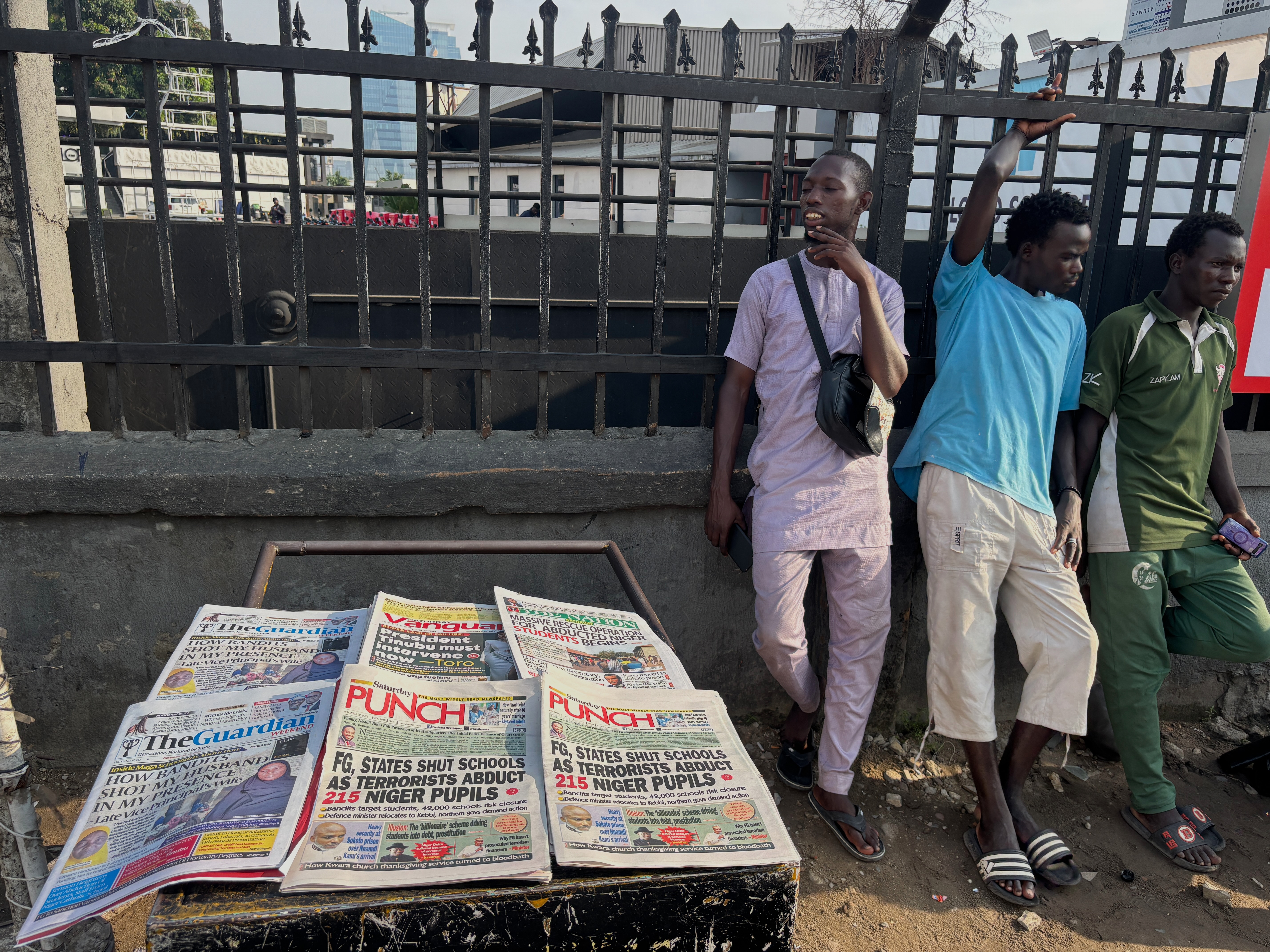 caption: People stand near a display local newspapers on the street of Lagos with headlines on gunmen abducting schoolchildren and staff of the St. Mary's Catholic Primary and Secondary School in Papiri community in Nigeria, Saturday, Nov. 22, 2025.