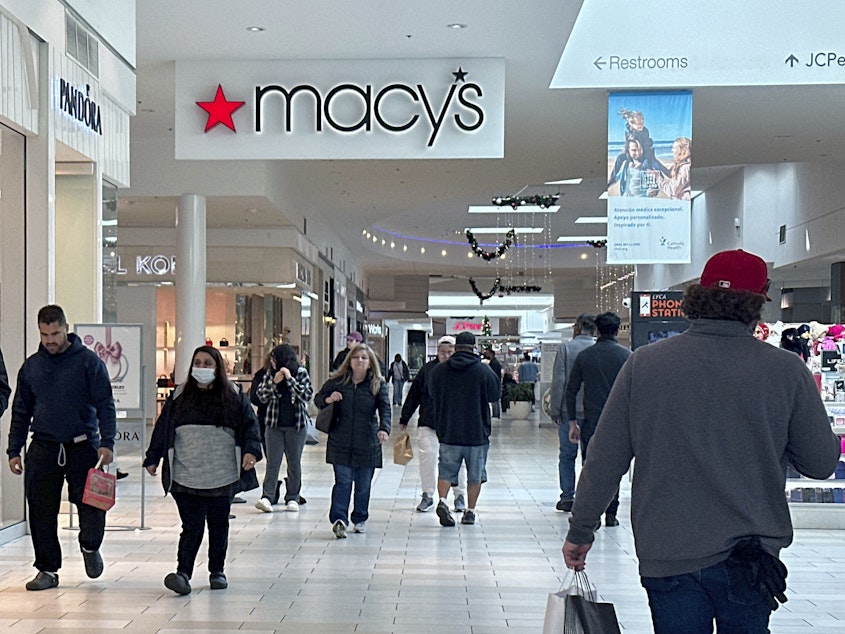 caption: Shoppers walk by a sign for the Macy's department store at a mall in Long Island, N.Y.