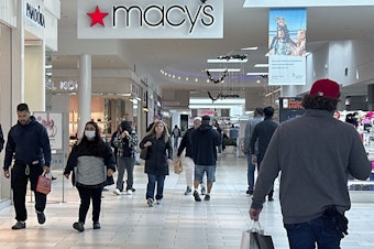 caption: Shoppers walk by a sign for the Macy's department store at a mall in Long Island, N.Y.