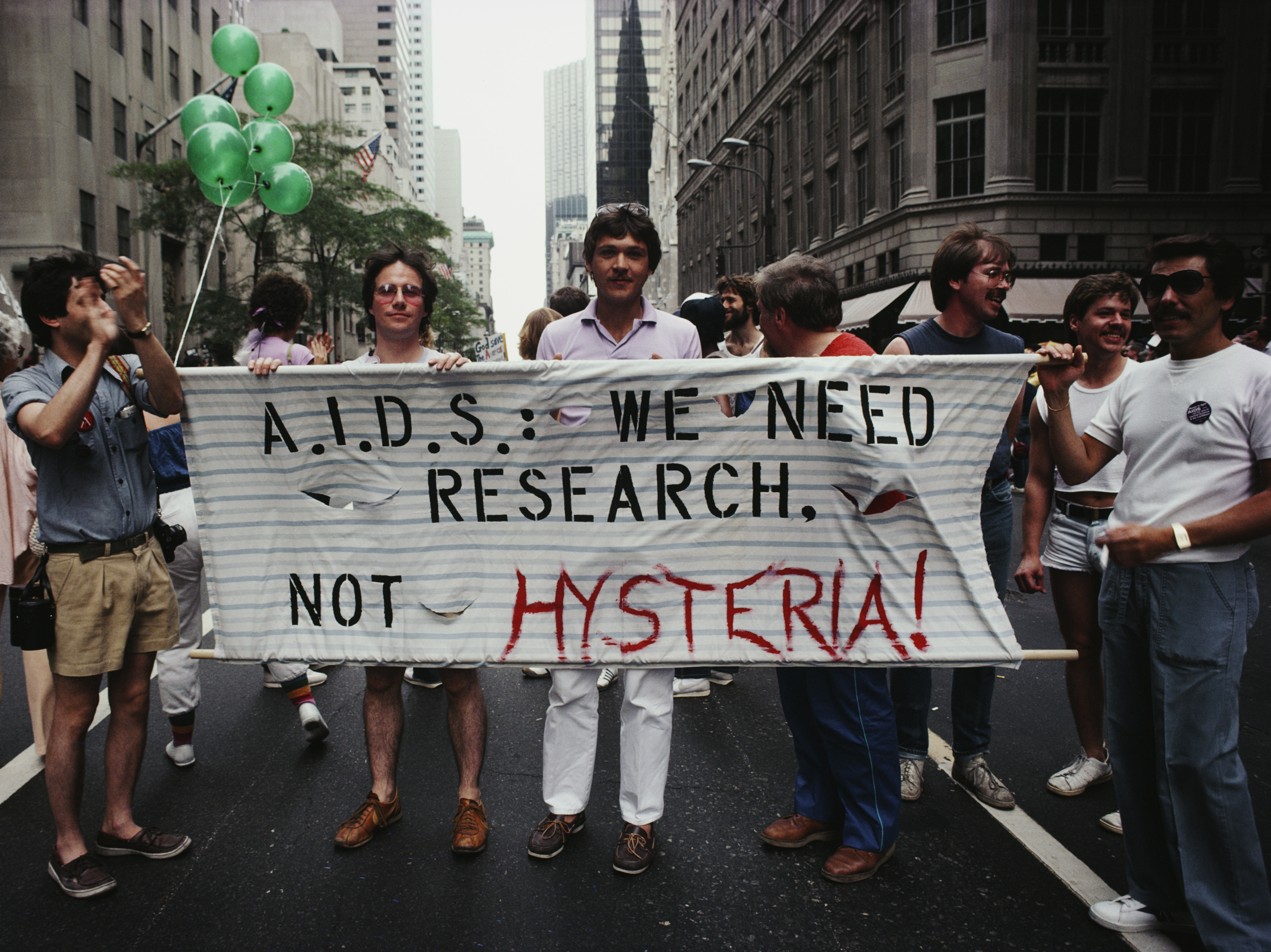 caption: Marchers on a Gay Pride parade through Manhattan, New York City, carry a banner which reads 'A.I.D.S.: We need research, not hysteria!', June 1983.