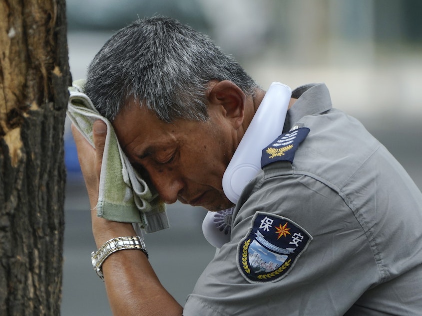 caption: A security guard wipes sweat from his brow in Beijing, on July 3, 2023. Record-breaking heat is unfolding around the world because of human-caused climate change and the cyclic climate pattern El Niño.
