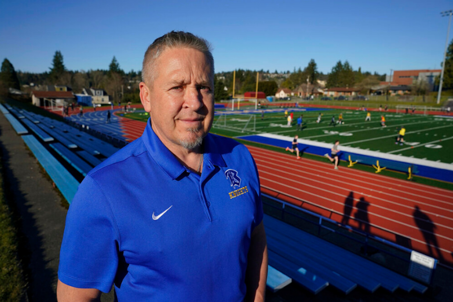 caption: Joe Kennedy, a former assistant football coach at Bremerton High School, poses for a photo March 9, 2022, at the school's football field. He was fired after refusing to stop kneeling in prayer with players and spectators on the field immediately after football games. He sued over the matter and took the case to the U.S. Supreme Court, arguing the Bremerton School District violated his First Amendment rights. 