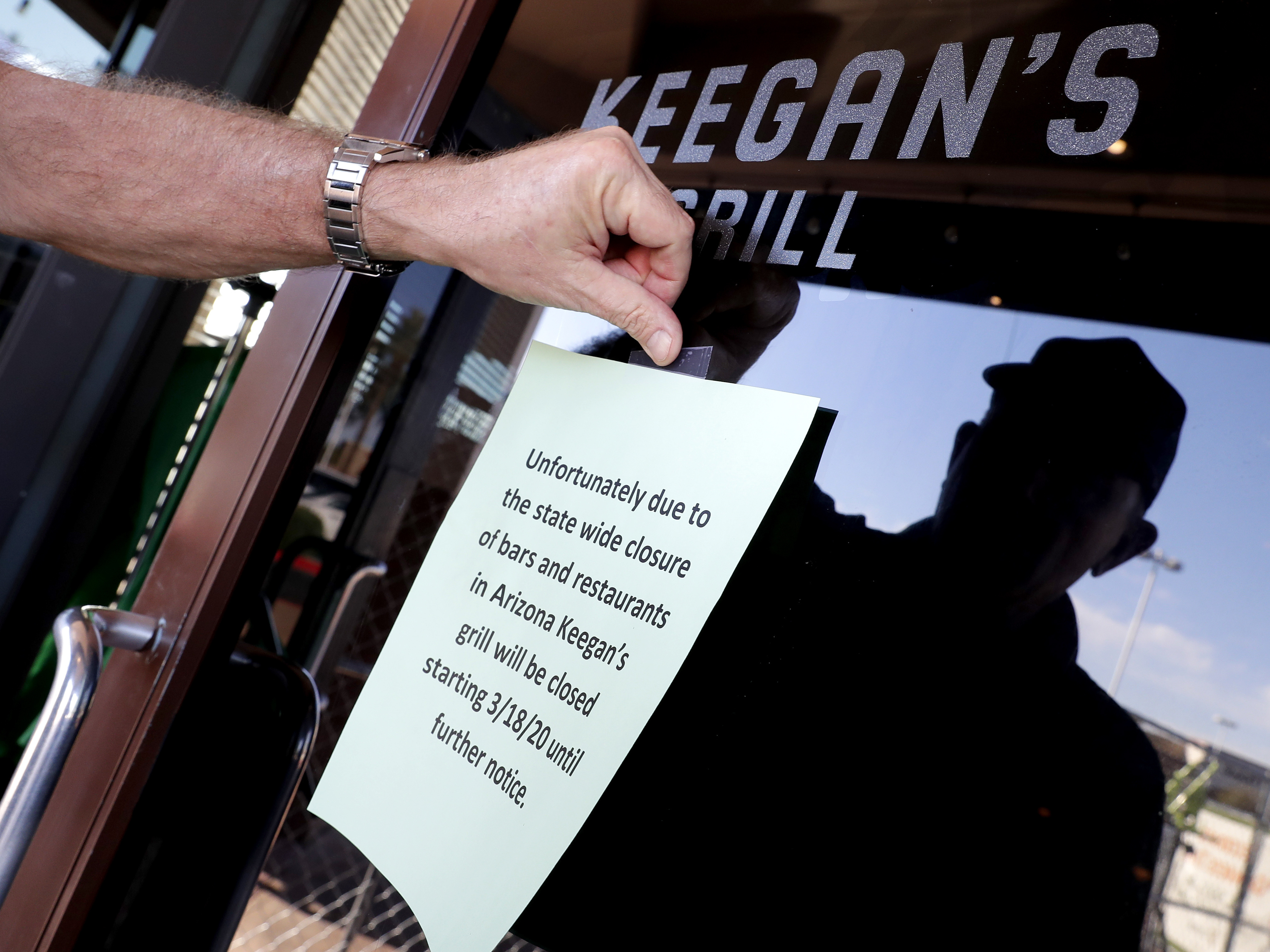 caption: Owner Steve Johnson attaches a notice on the door of Keegan's Grill in Phoenix notifying guests his restaurant will close. Rapid shutdowns have delivered a blow to restaurants around the country.