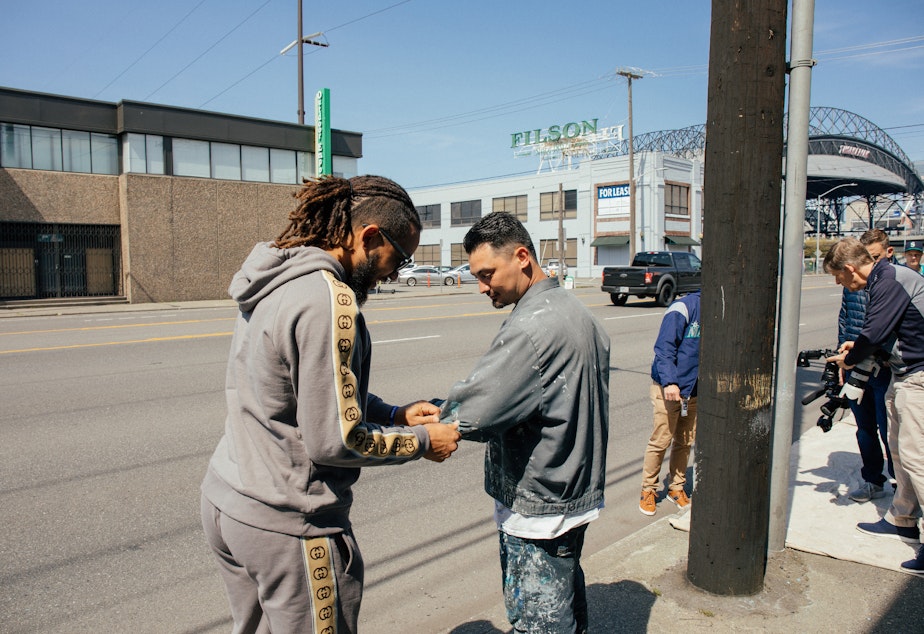 caption: Mariners shortstop J.P. Crawford wipes wet paint from his hands onto muralist Alexander Codd on Saturday, April 23, 2022.