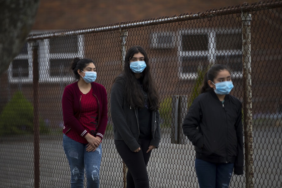 caption: From left, sisters Mia Hurtado, 14, Miliani Hurtado, 12, and Marleni Hurtado, 10, wait in line for walk and drive through confessions with Father Jose Alvarez on Friday, April 24, 2020, in the parking lot at Holy Family Roman Catholic Church in White Center. 