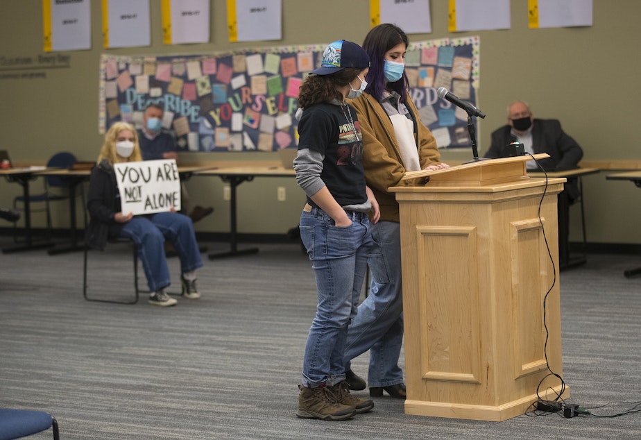 caption: Ballard High School student Cass Sylves, left, stands in support of Rosa Basiji, right, as she stands before the Seattle Public Schools school board and shares her experience, on Wednesday, December 1, 2021, in Seattle. 