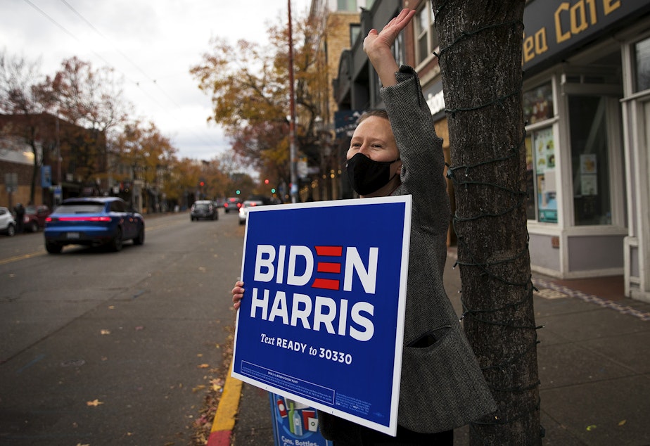 caption: Brittney Moraski holds a Biden-Harris sign as cars honk their horns shortly after Biden was officially named the president elect on Saturday, November 7, 2020, at the intersection of East Olive Way and Broadway East in Seattle.
