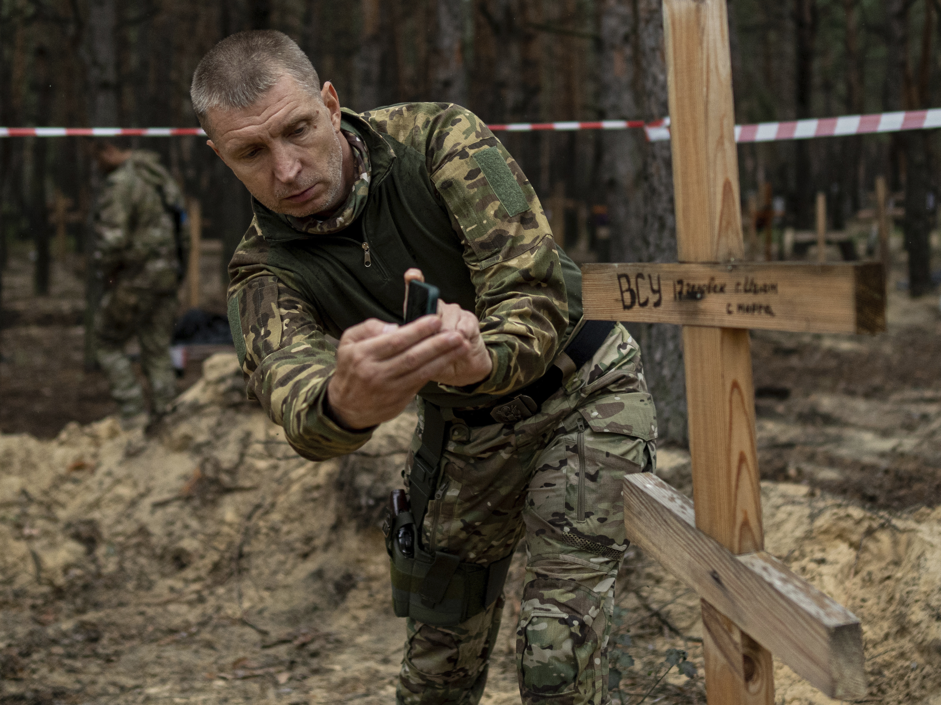 caption: Oleg Kotenko, the commissioner for issues of missing persons under special circumstances, uses his smartphone to film the grave a Ukrainian soldier in the recently retaken area of Izium, Ukraine, Sept. 15, 2022.