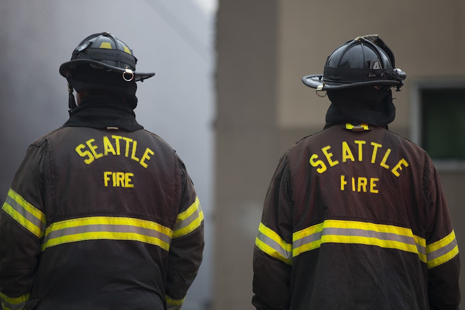 caption: Seattle firefighters work to put out a fire on Monday, October 7, 2019, at the intersection of NW Market Street and 24th Avenue Northwest in Seattle.