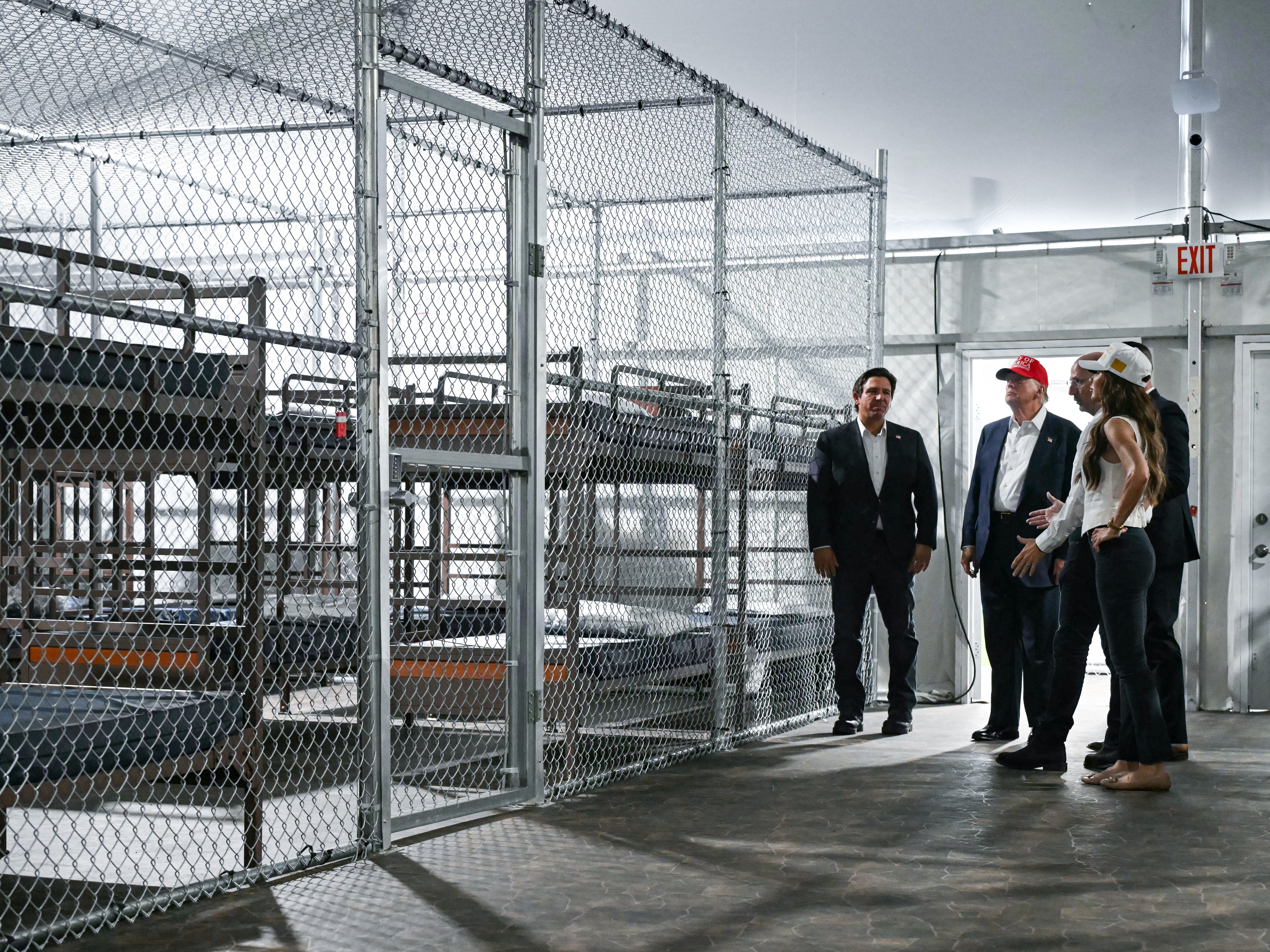 caption: President President Donald Trump (second from left), Florida Governor Ron DeSantis (L), and Secretary of Homeland Security Kristi Noem (R) tour a migrant detention center, dubbed "Alligator Alcatraz," located at the site of the Dade-Collier Training and Transition Airport in Ochopee, Fla. on July 1, 2025.
