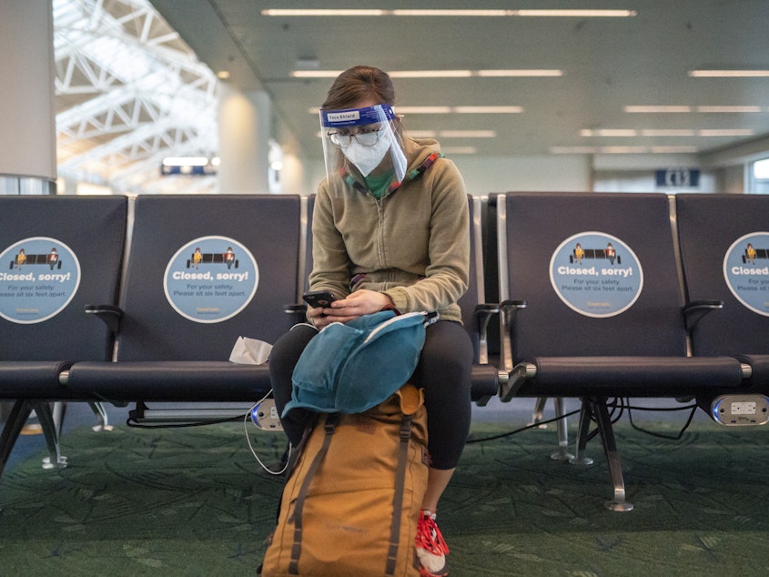 caption: A traveler waits for a flight at Portland International Airport in Oregon last week. Public health experts say it's important that people who traveled or gathered with others are especially careful over the next two weeks.