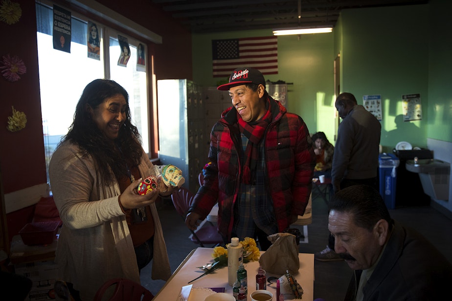 caption: Humberto Ramos, center, laughs with Lucina Carrillo, left, while preparing their Day of the Dead altar on Tuesday, October 29, 2019, at Casa Latina in Seattle.