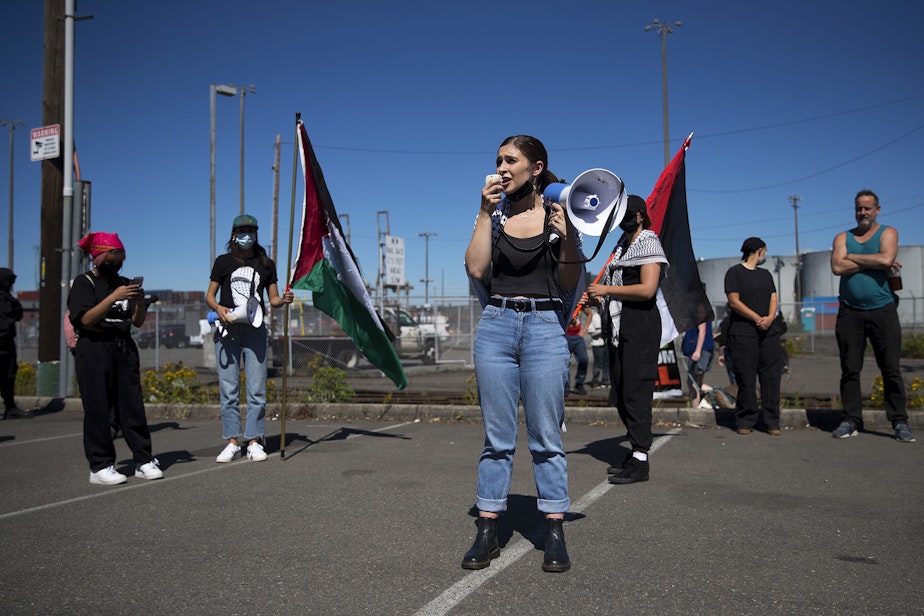 caption: Aisha Mansour, a representative of Palestinian feminist organization Falastiniyat, leads a chant before blocking an intersection in protest of the Israeli Zim San Diego Vessel, on Thursday, June 17, 2021, at the Port of Seattle. "By blocking Zim from unloading at our port, we have made clear that the city of Seattle does not welcome any business that profits from apartheid or human rights violations," said Mansour.