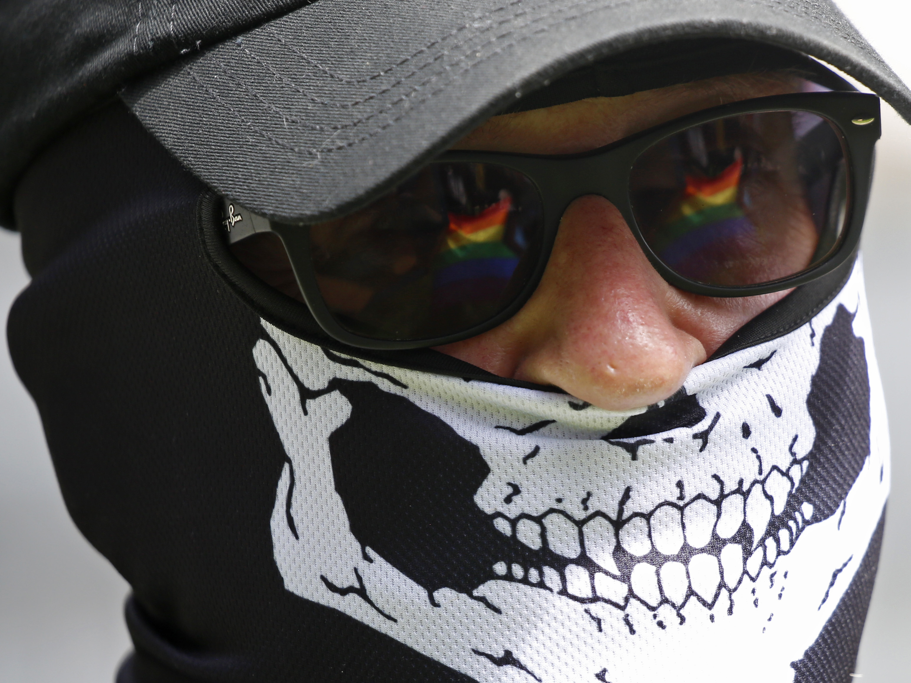 caption: The Pride flag is reflected in the glasses of a white nationalist who came to protest at the LGBTQ+ community's "Pride in the Park" event in Coeur d'Alene, Idaho, on June 11, 2022.