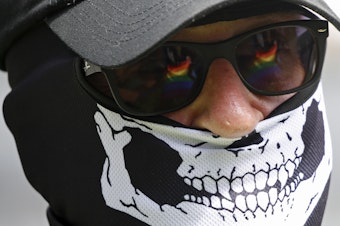 caption: The Pride flag is reflected in the glasses of a white nationalist who came to protest at the LGBTQ+ community's "Pride in the Park" event in Coeur d'Alene, Idaho, on June 11, 2022.