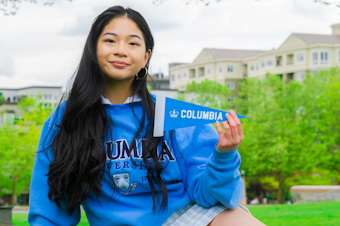 caption: Khanh Doan poses in a Columbia University sweatshirt holding up a Columbia University flag in May 2021.
